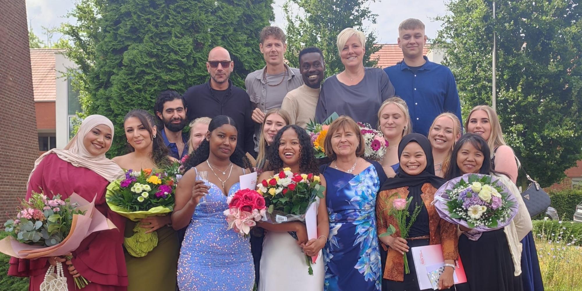 Absolventinnen und Absolventen der Ausbildung zur Pflegefachfrau beziehungsweise zum Pflegefachmann halten Blumen in den Händen und schauen in die Kamera.